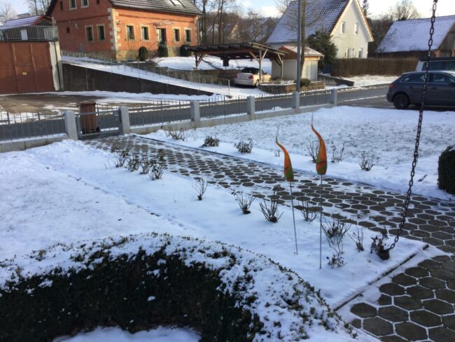 Eingangsbereich vorher Vorgarten im Winter mit Schneedecke auf Rasen und Pflasterweg. Der Weg ist mit sechseckigen Steinen gepflastert.